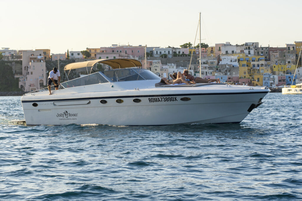 Itama yacht with guests sunbathing while sailing near a waterfront residential community